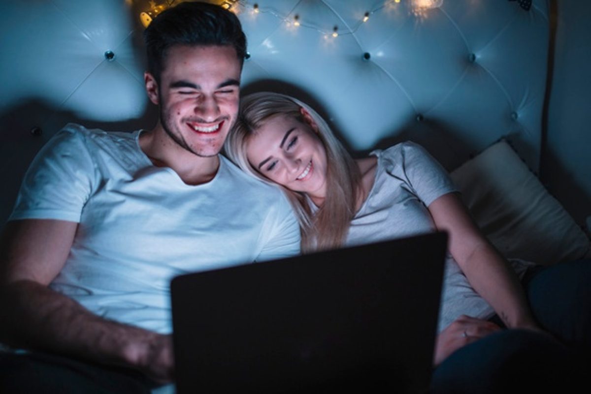 smiling-couple-watching-film-bed_23-2147771152